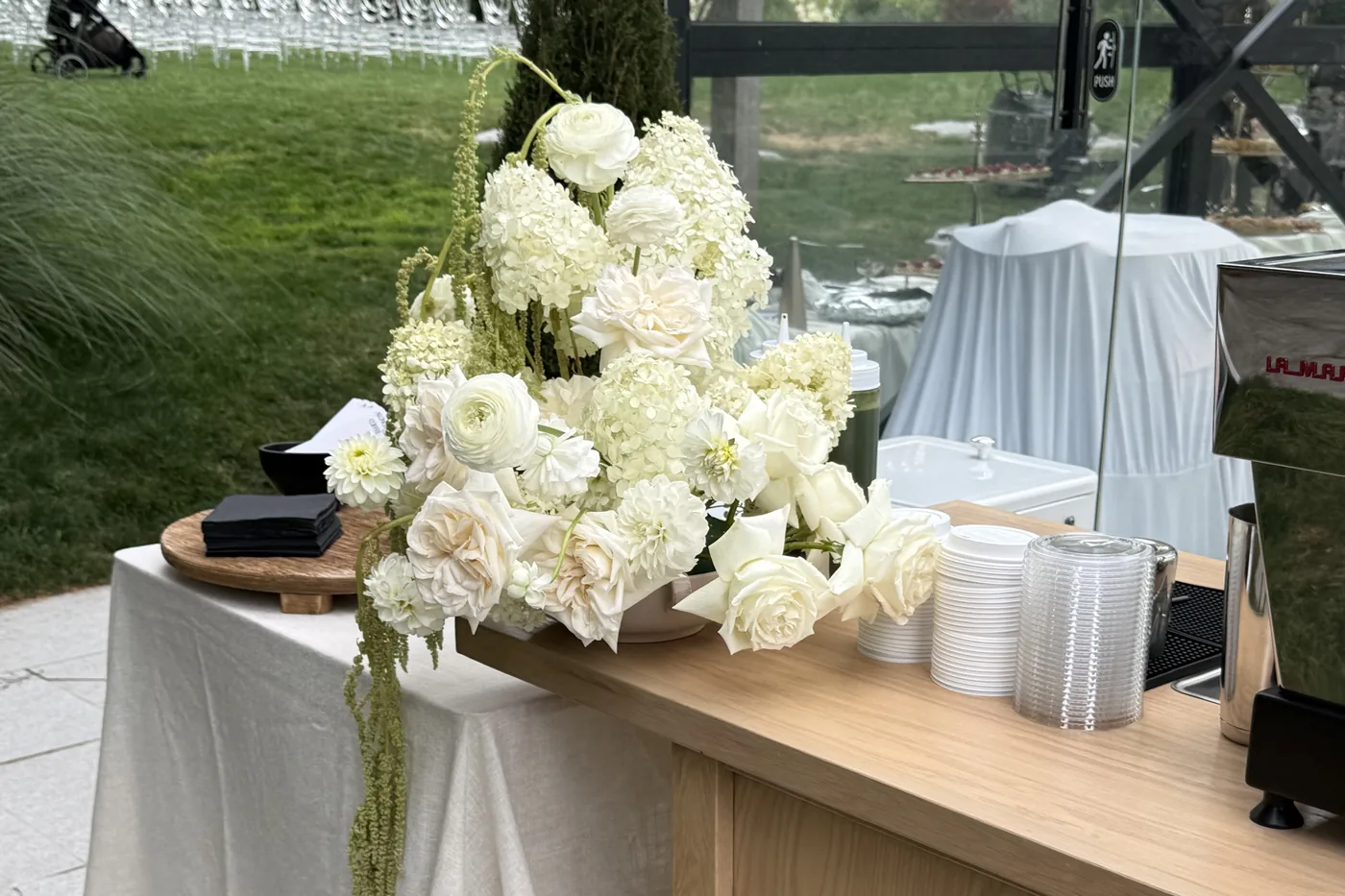 The Alongside espresso cart with white florals inside the Glass Venue at Paradise Village, ceremony chairs visible through the glass wall